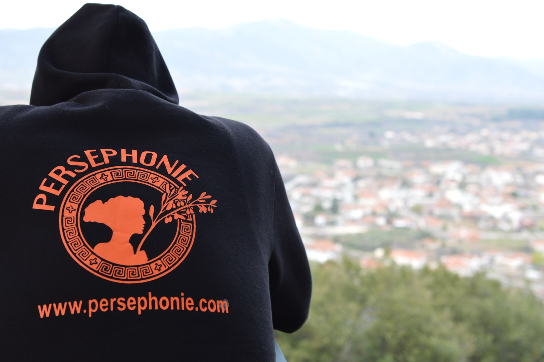 Rückenansicht eines schwarzen Hoodies mit dem Persephonie-Zeichen in Orange